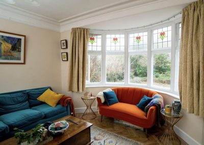 Large sitting room with colourful sofas and cushions and a large bay window with Granada Secondary glazing installed